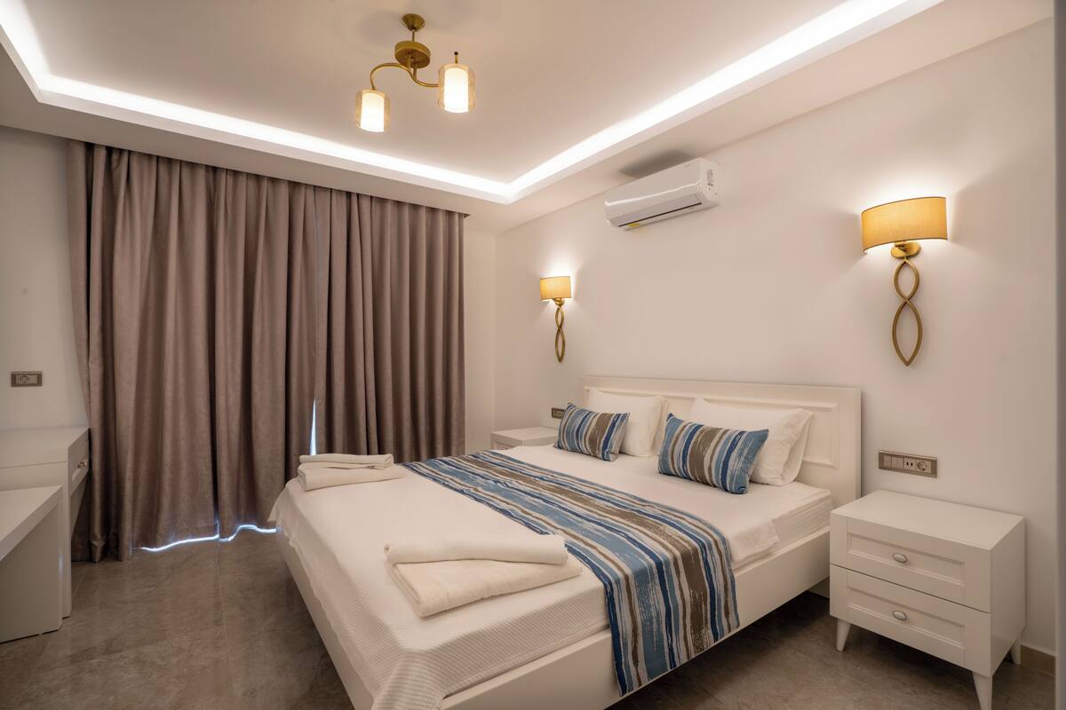 A modern hotel room with a large bed, bedside tables, a desk, and a ceiling light fixture.