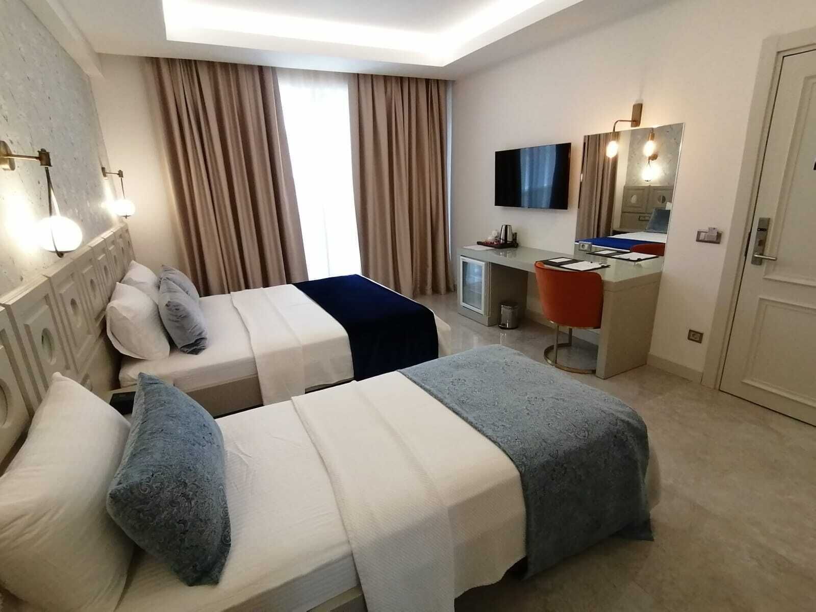 Habitación de hotel con dos camas, un escritorio, una silla, un televisor y un espejo.