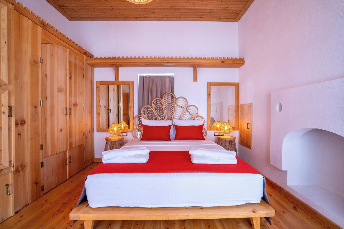 A wooden-framed bedroom with a large bed, wooden wardrobe, and two bedside lamps.