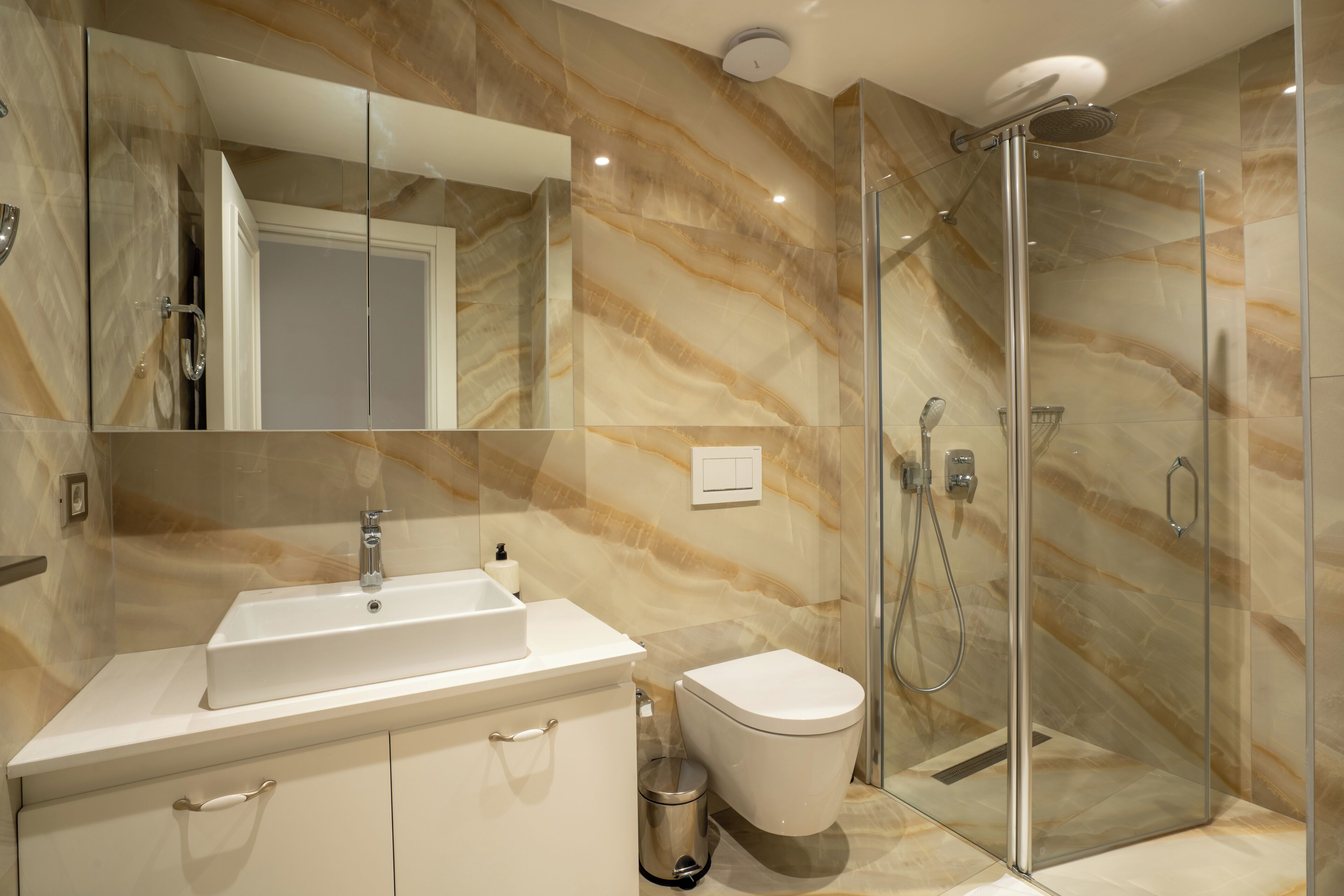 A modern bathroom with a marble backsplash, a glass shower enclosure, and a white sink.