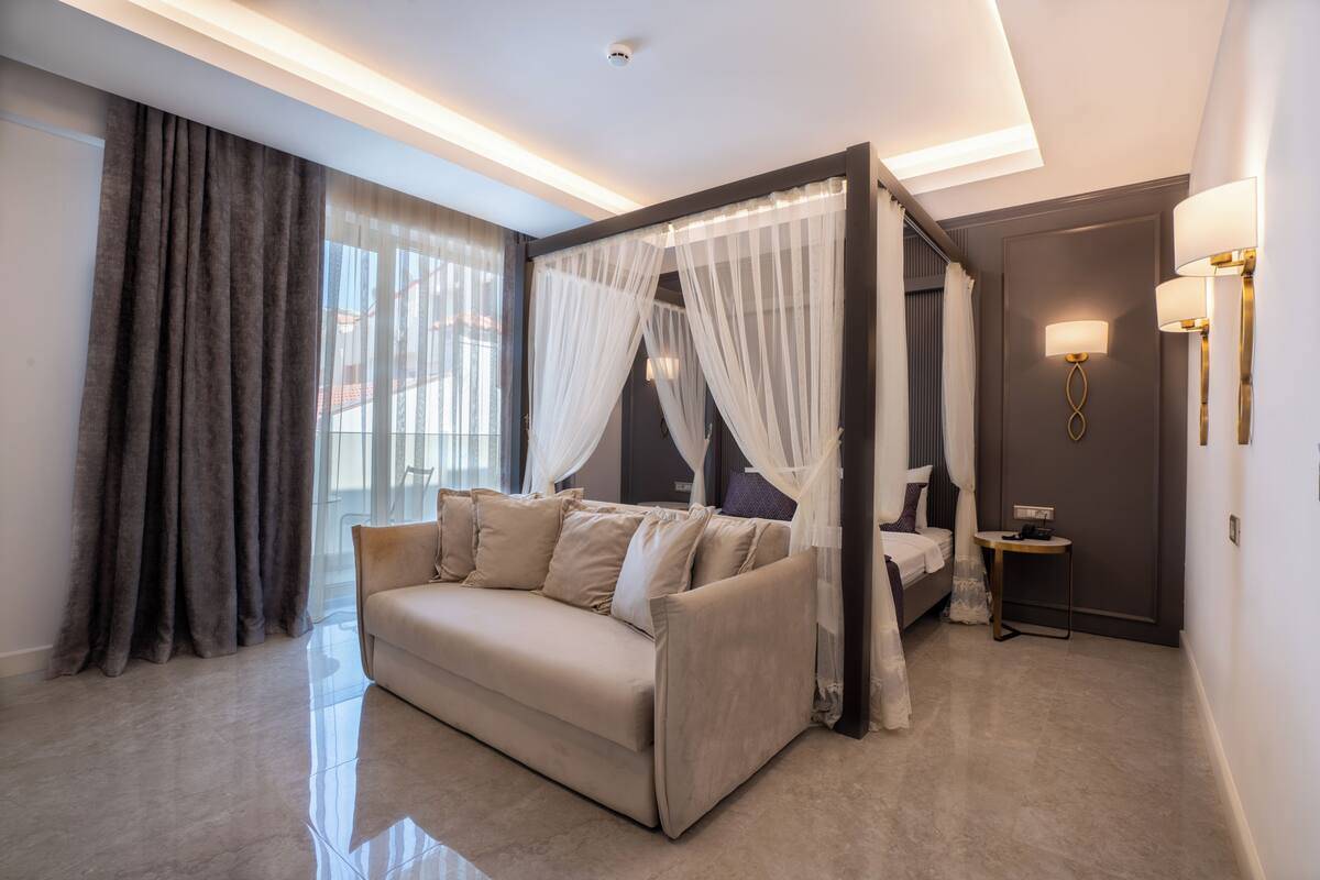 A modern bedroom with a four-poster bed, a sofa, and a bedside table.