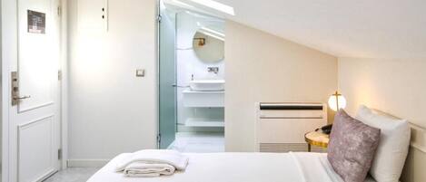 A hotel room with a neatly made bed, a bedside table with a lamp, and a view of the bathroom through an open door.