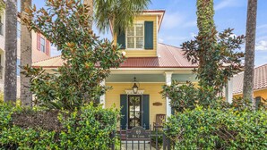 A yellow house with a green door and shutters, surrounded by lush greenery and palm trees. - Home with Pool in the Gated Community of Caribe (Destin)