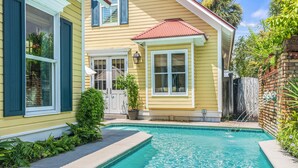 A residential property with a swimming pool, a brick wall, and a yellow house with blue shutters. - Home with Pool in the Gated Community of Caribe (Destin)