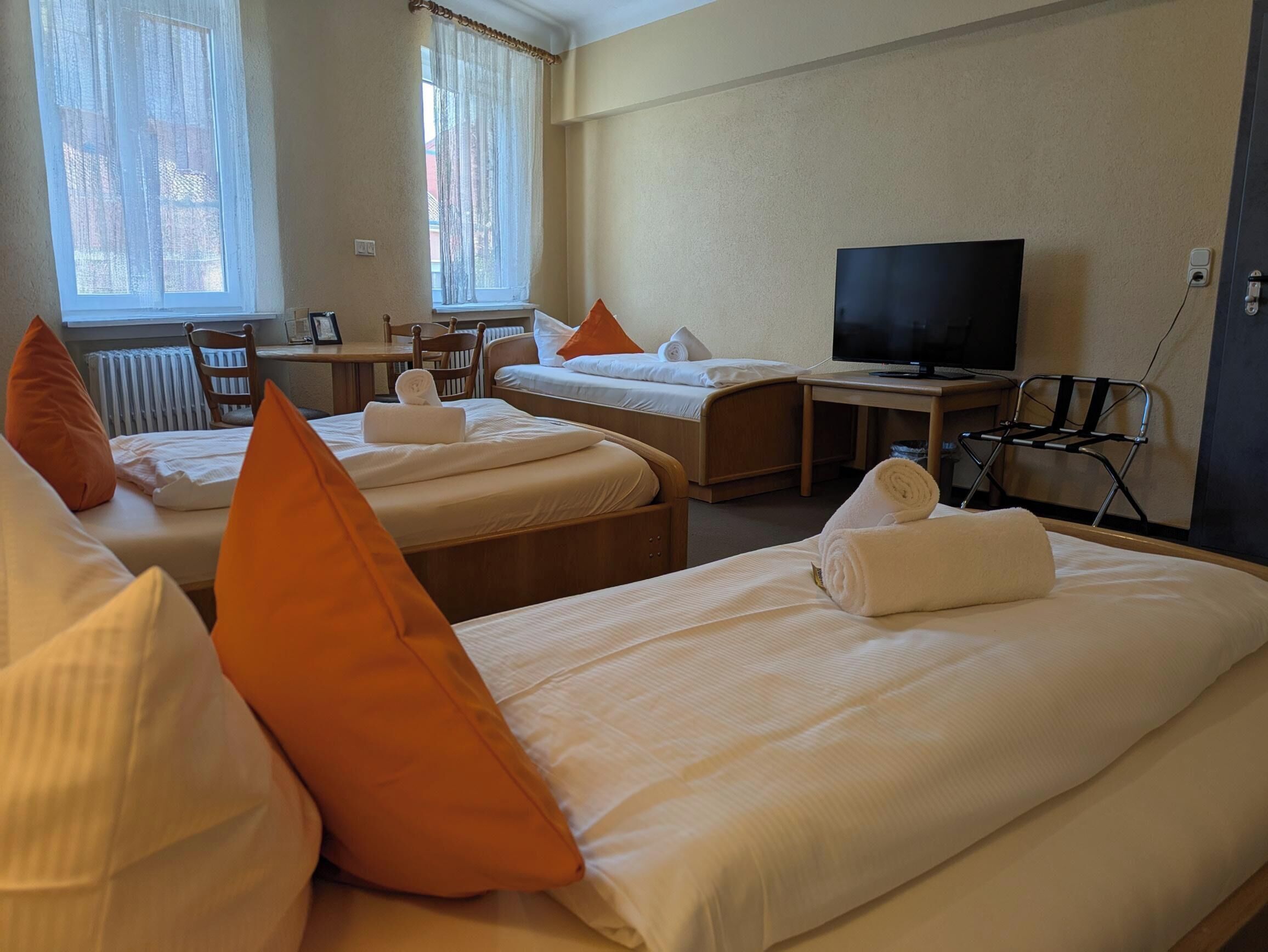 A hotel room with two beds, a desk, a chair, a television, and a window with curtains.
