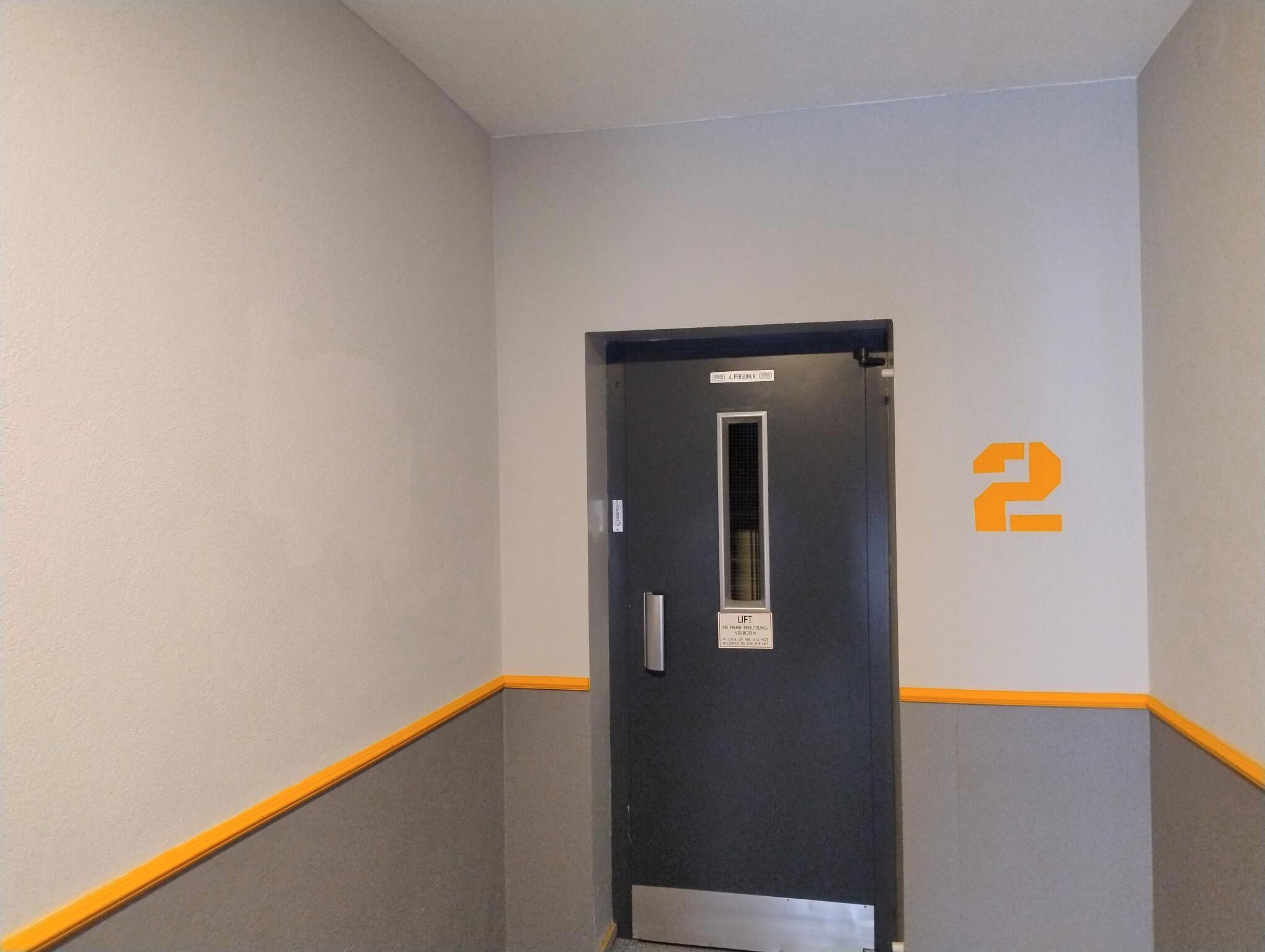 A narrow hallway with a door marked '2' and a lift sign indicating a lift for 4 persons.