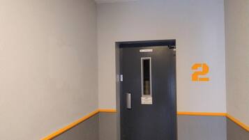 Un couloir étroit avec une porte portant le numéro « 2 » et un panneau indiquant la présence d’un ascenseur pouvant accueillir quatre personnes.