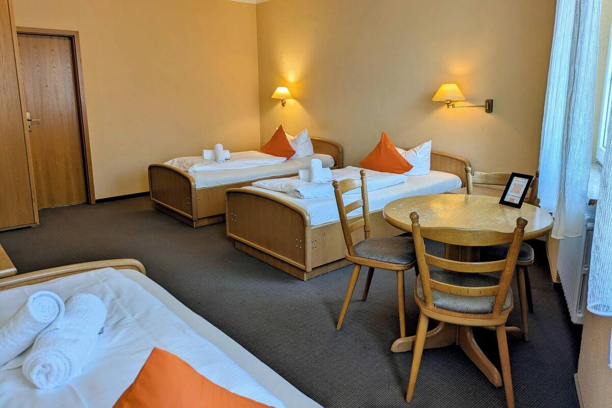 A hotel room with two single beds, a round table with chairs, and a door.