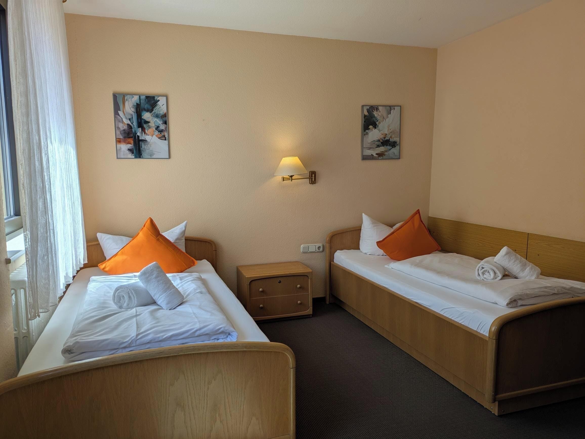 Habitació d'hotel amb dos llits individuals, una meseta de nit, una làmpada i dos quadres a les parets.