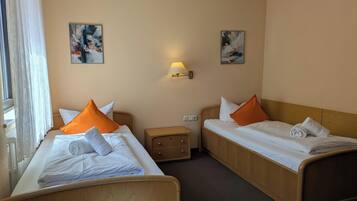 A hotel room with two single beds, a nightstand, a lamp, and two paintings on the walls.