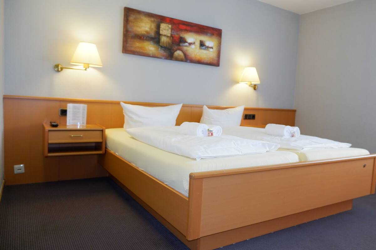 A hotel room with a large bed, two bedside lamps, a nightstand, and a painting on the wall.