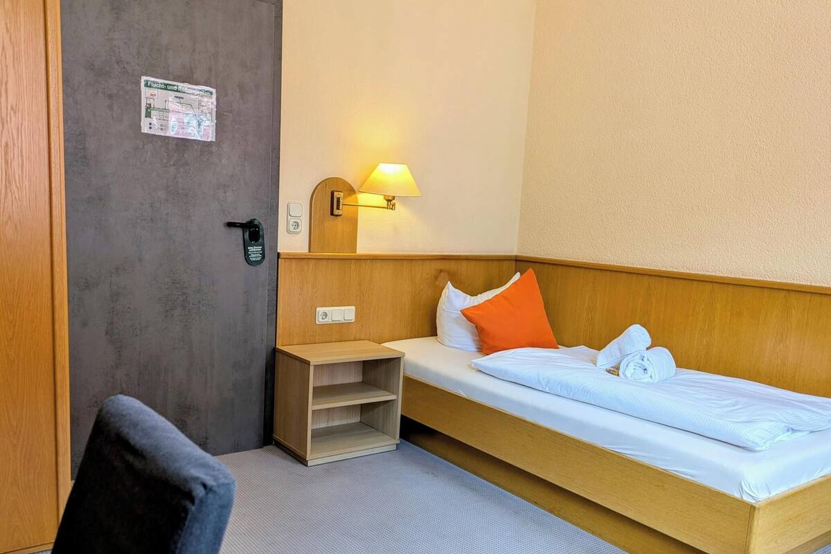 A hotel room with a bed, a nightstand, a lamp, and a chair.