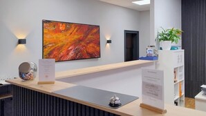 Zona de recepción de hotel con diseño moderno, que incluye un mostrador de recepción, un cuadro abstracto grande en la pared y una planta en maceta.