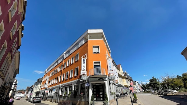 Un hotel de varios pisos con una fachada naranja destacada, múltiples ventanas y una entrada a nivel de calle.