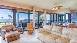 A spacious living area with a large window overlooking a golf course and the ocean, featuring a beige sofa, a leather armchair, and a wooden coffee table.