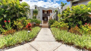A modern building with a central staircase, surrounded by lush tropical plants and a clear sky.