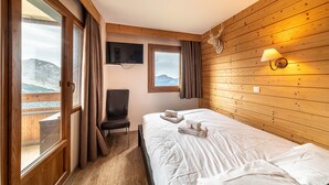 Una habitación con cama, sillón, televisión y ventana con cortinas.