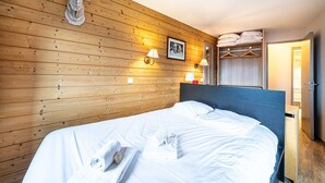 Una habitación con paneles de madera, una cama con ropa de cama blanca, cabecero, lámparas de noche, una foto enmarcada y un armario con espacio para colgar.