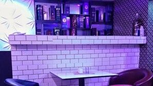 A bar area with a white tiled wall, a counter with liquor bottles, and colorful seating. - Chukzie Suites & Apartments (Lagos)