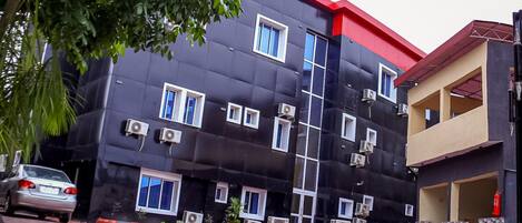 Un edificio de varios pisos con fachada negra y techo rojo. Se observan múltiples ventanas y unidades de aire acondicionado adheridas a las paredes exteriores.
