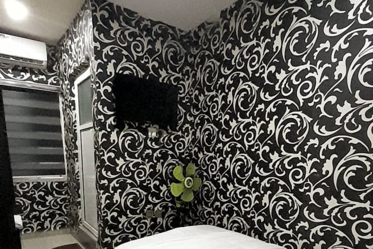 A bedroom with a bed, a TV mounted on the wall, and a patterned wallpaper.