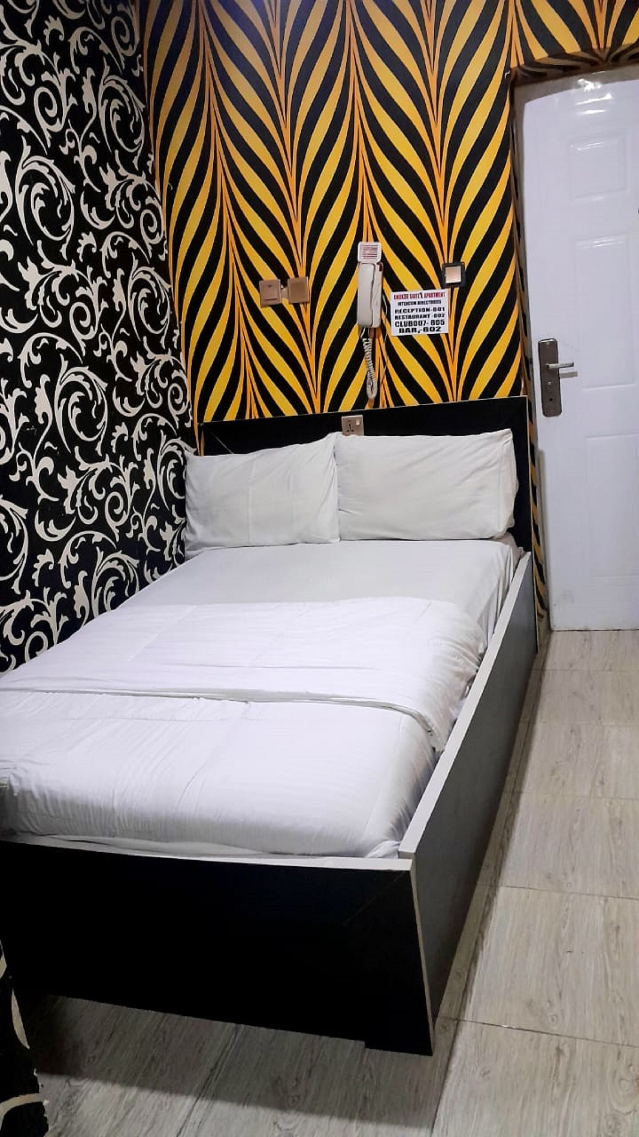 A bed with a black frame and white bedding in a room with patterned wallpaper and a door.