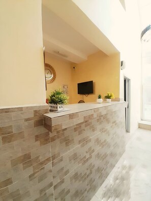 Uma área de recepção com parede revestida de azulejos, televisão de tela plana e plantas em vasos.