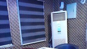 A room with a table and four chairs, a window with blinds, a wall-mounted air conditioner, and a small TV on the wall. - Chukzie Suites & Apartments (Lagos)
