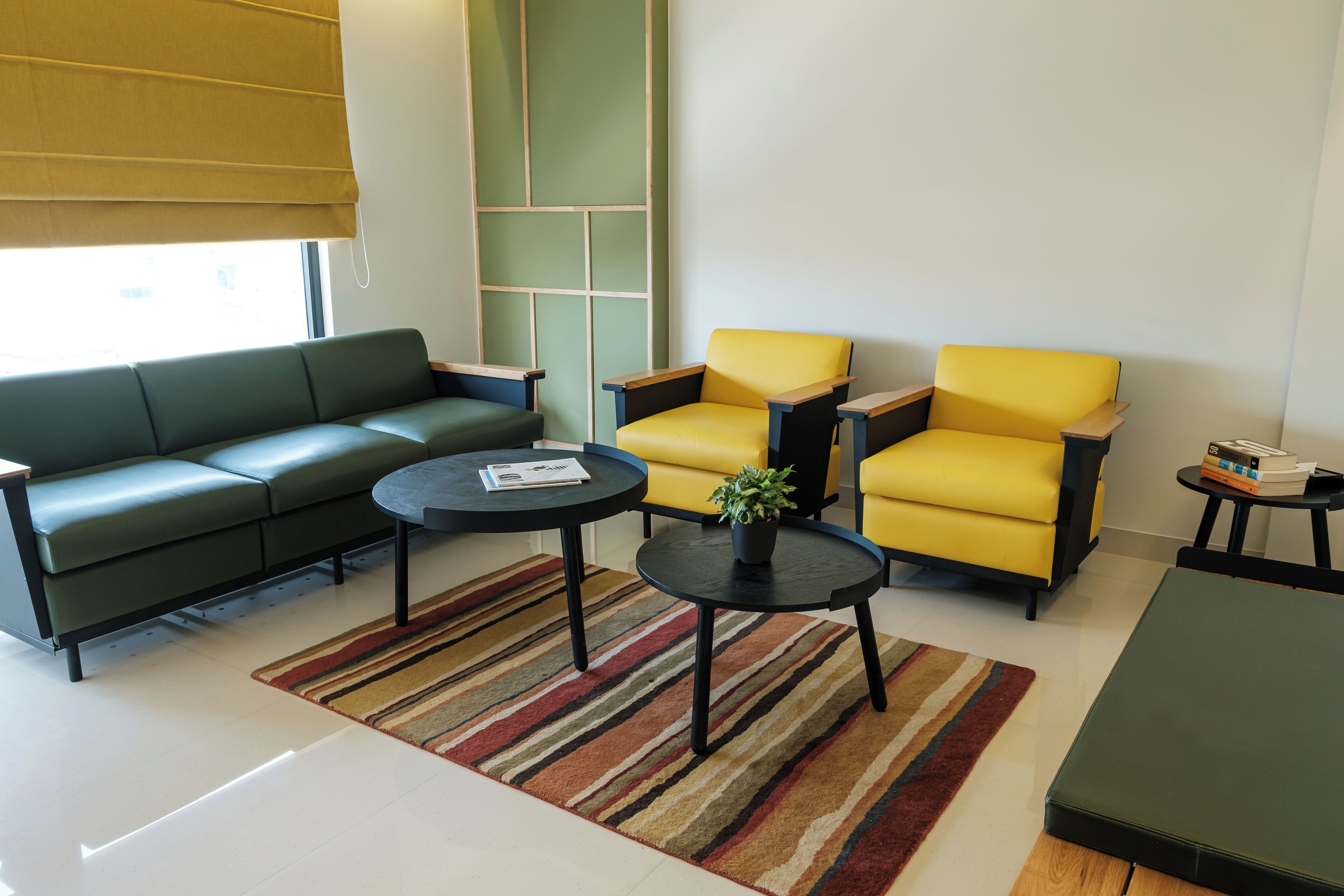 A modern living room with a green sofa, two yellow armchairs, a small round table, and a striped rug.