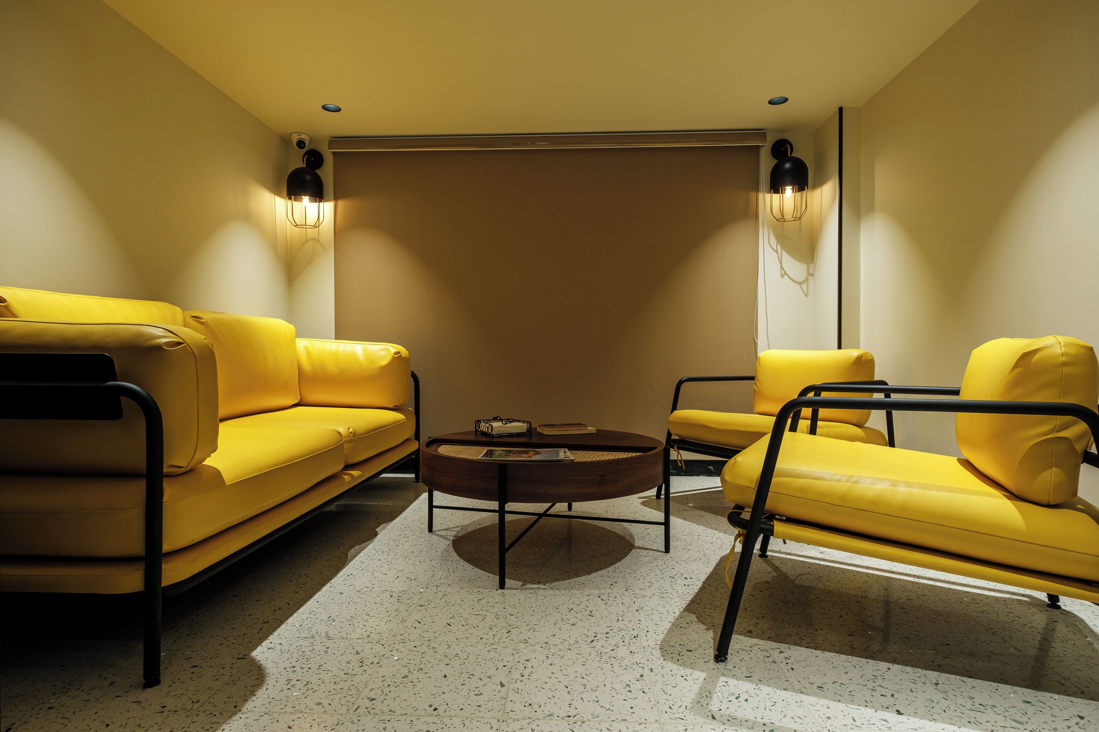 Een moderne woonkamer met gele banken, een ronde salontafel en zwarte metalen frames.