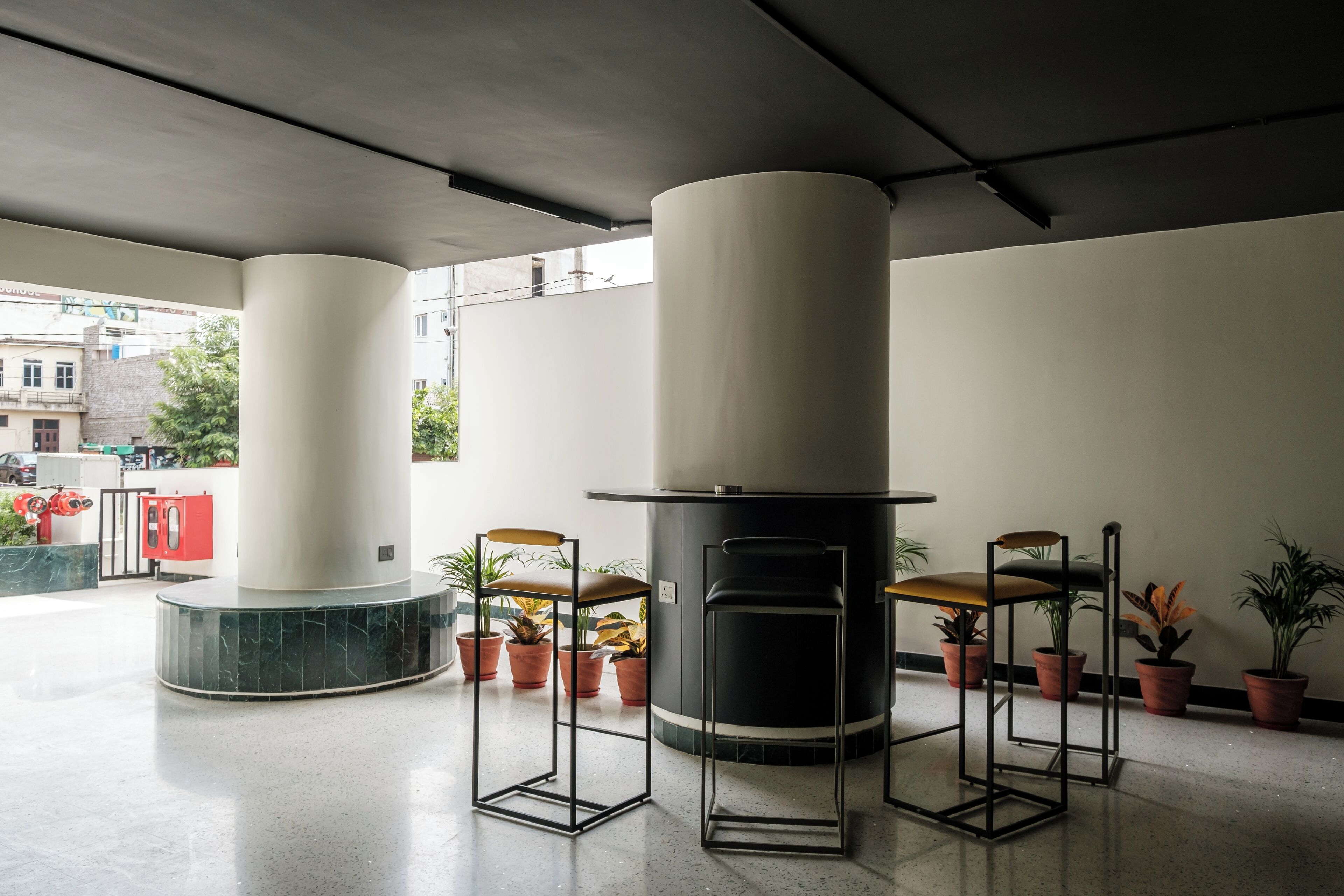A modern interior with two cylindrical pillars, a central black stove, and several potted plants.