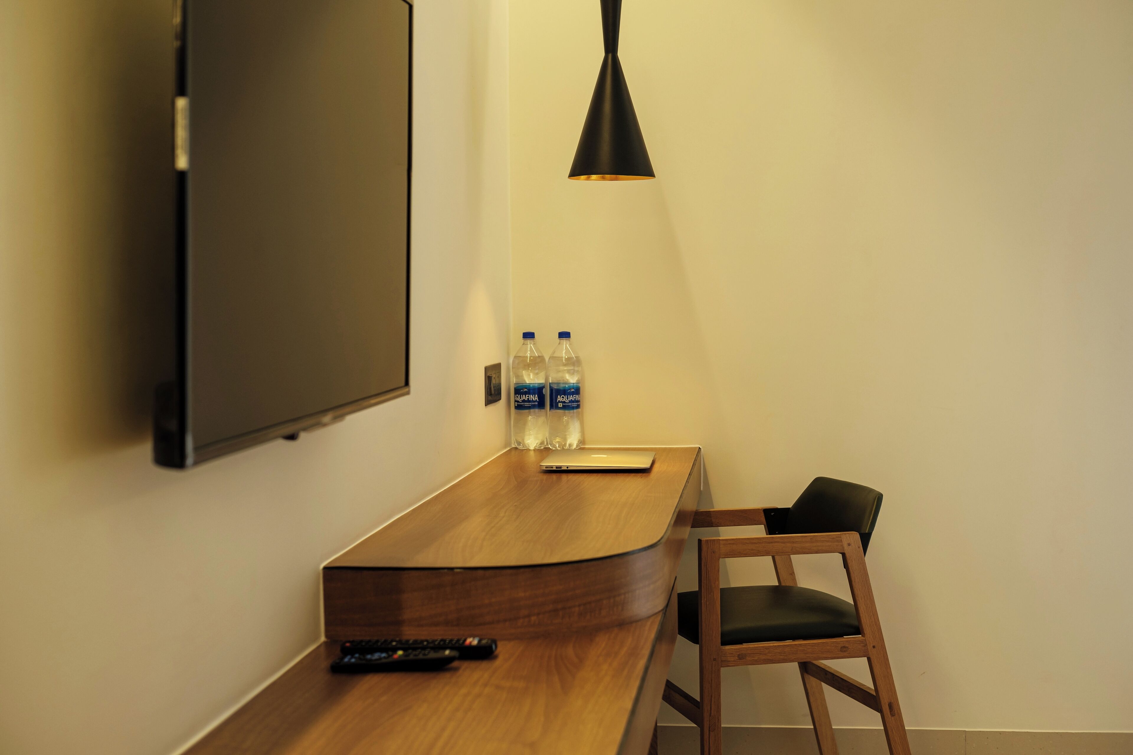 Habitación de hotel con un escritorio de madera, televisor montado, dos botellas de agua, un control remoto y una silla negra.