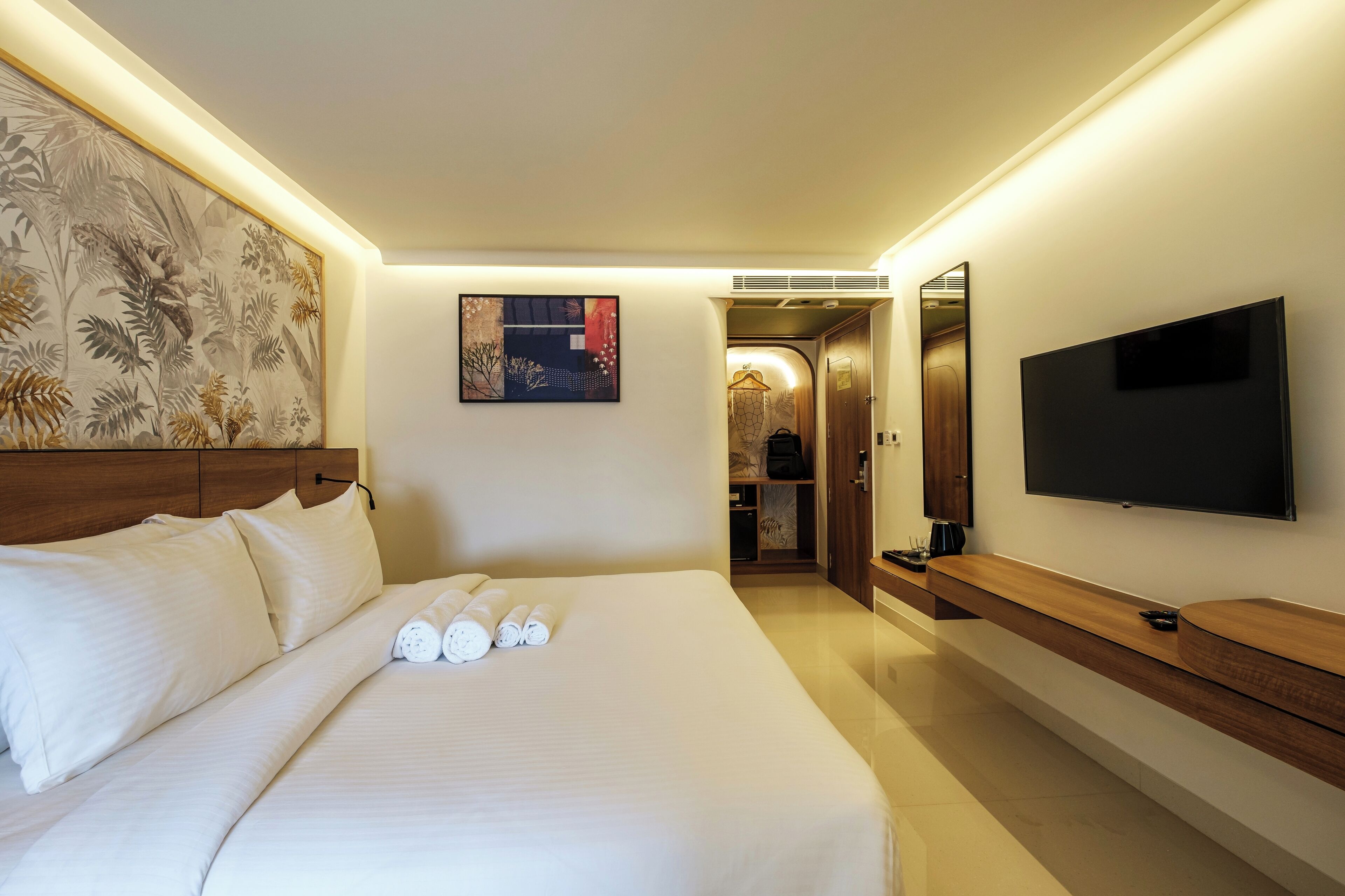 Une chambre d’hôtel avec un grand lit, un téléviseur à écran plat, un tableau au mur et une console en bois.