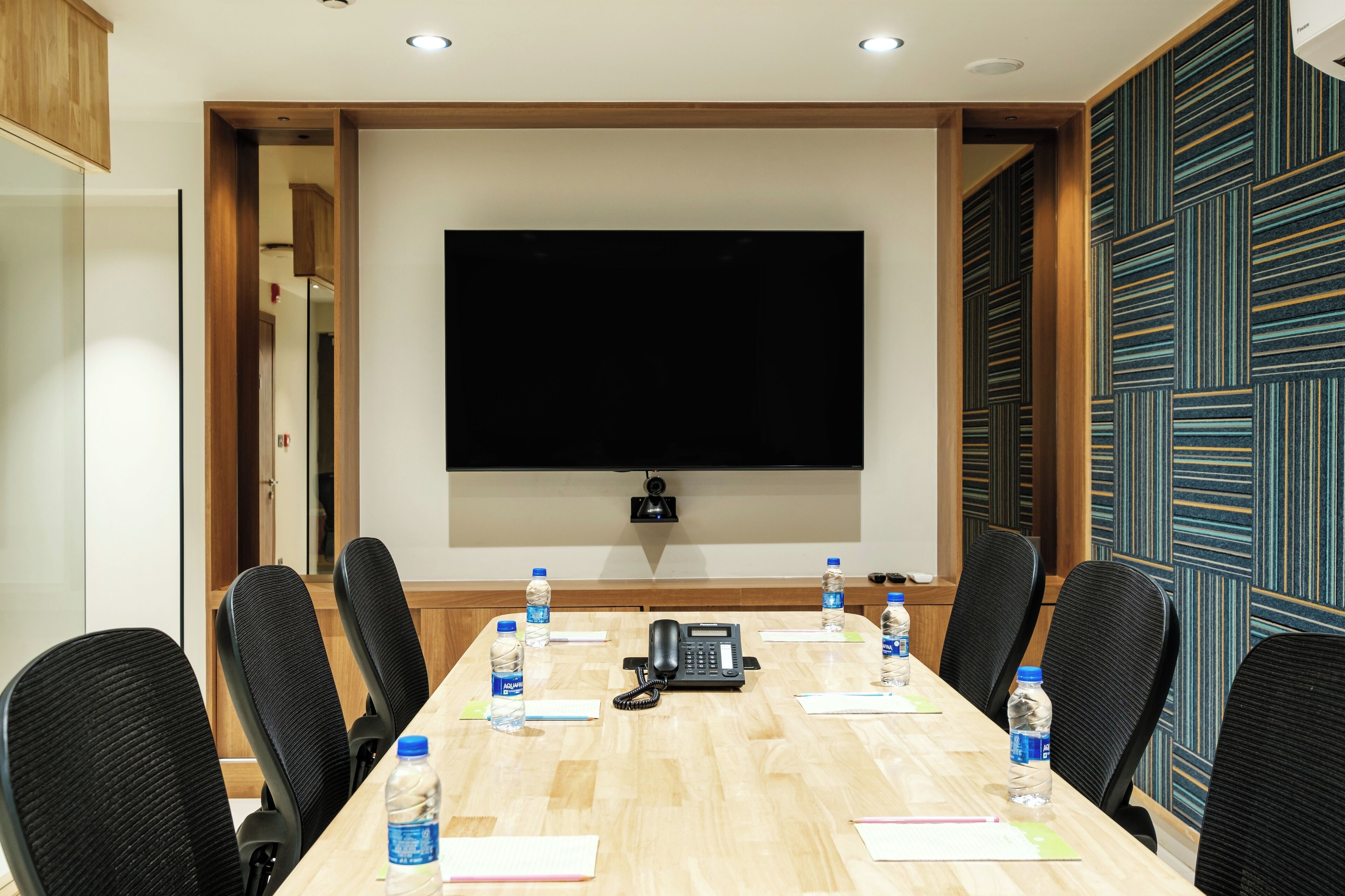 A conference room with a long table, black chairs, a phone, and water bottles.