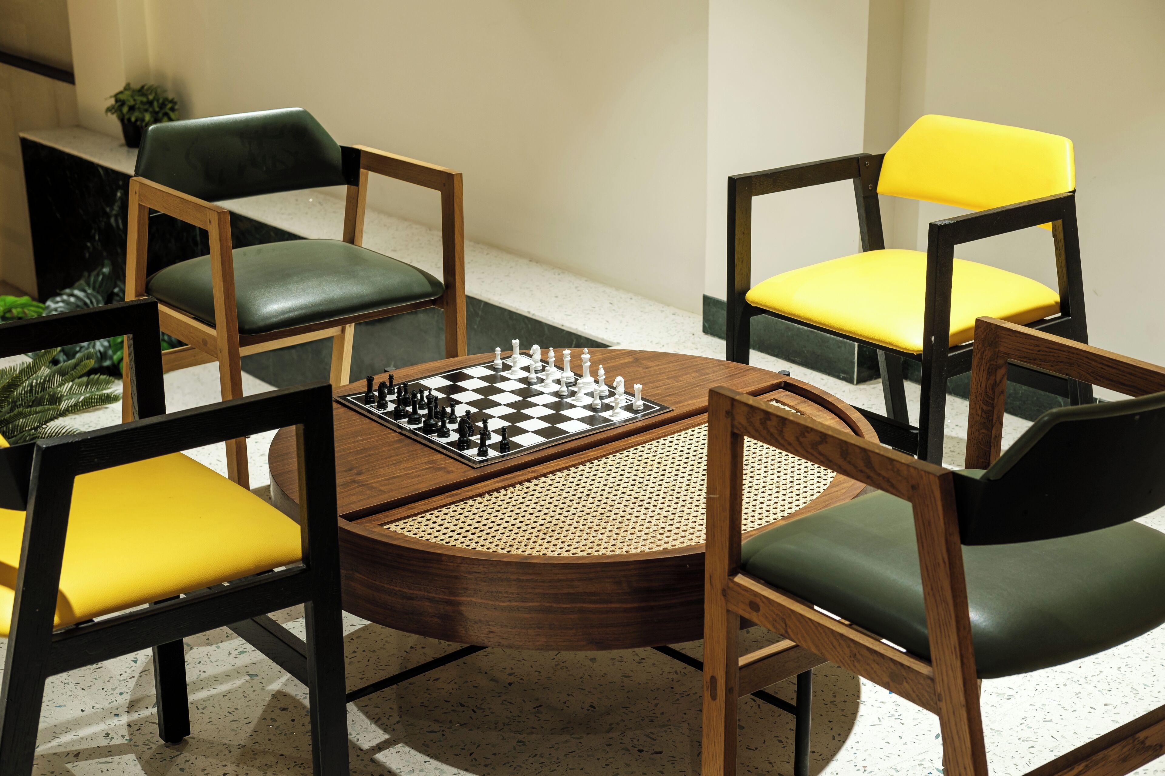 Una mesa de madera redonda con un tablero de ajedrez en el centro, rodeada por cuatro sillas con cojines amarillos y verdes.