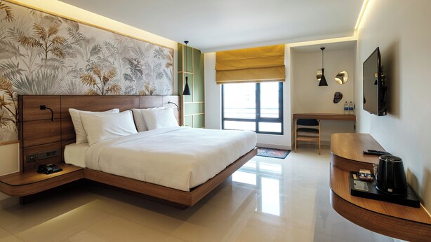 Una habitación de hotel moderna con una cama grande, un escritorio, un televisor y una obra de arte colgada en la pared.