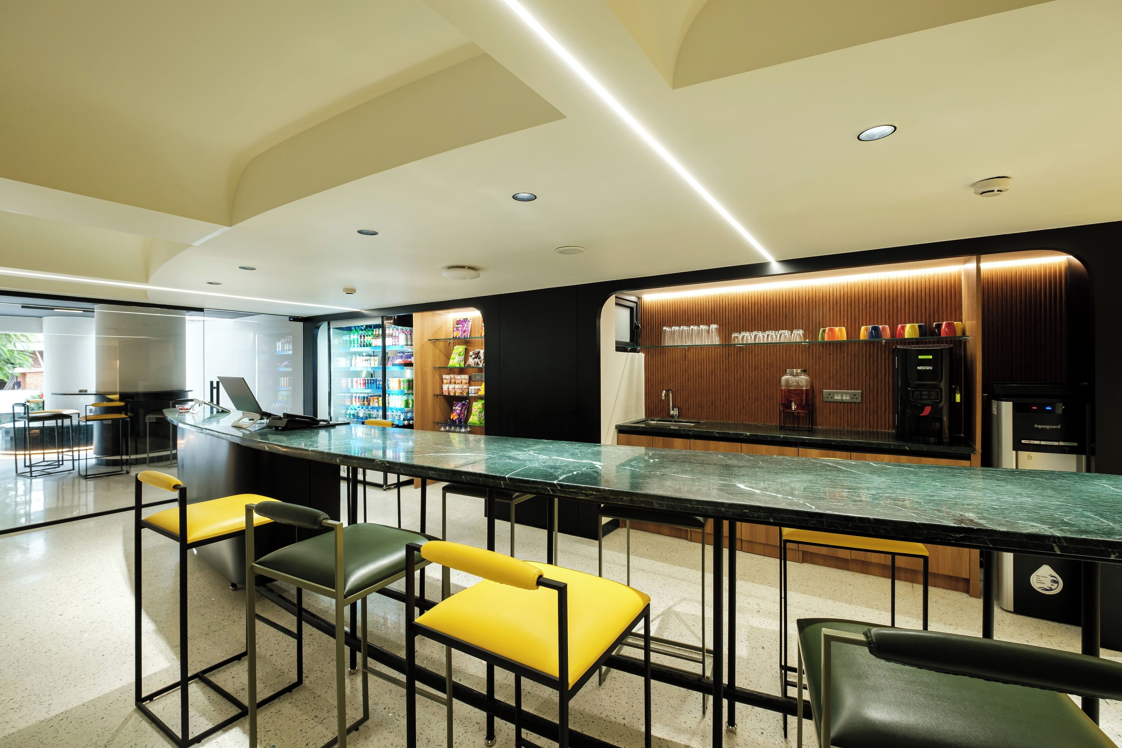 A modern bar area with a marble countertop, bar stools, and a beverage dispenser.