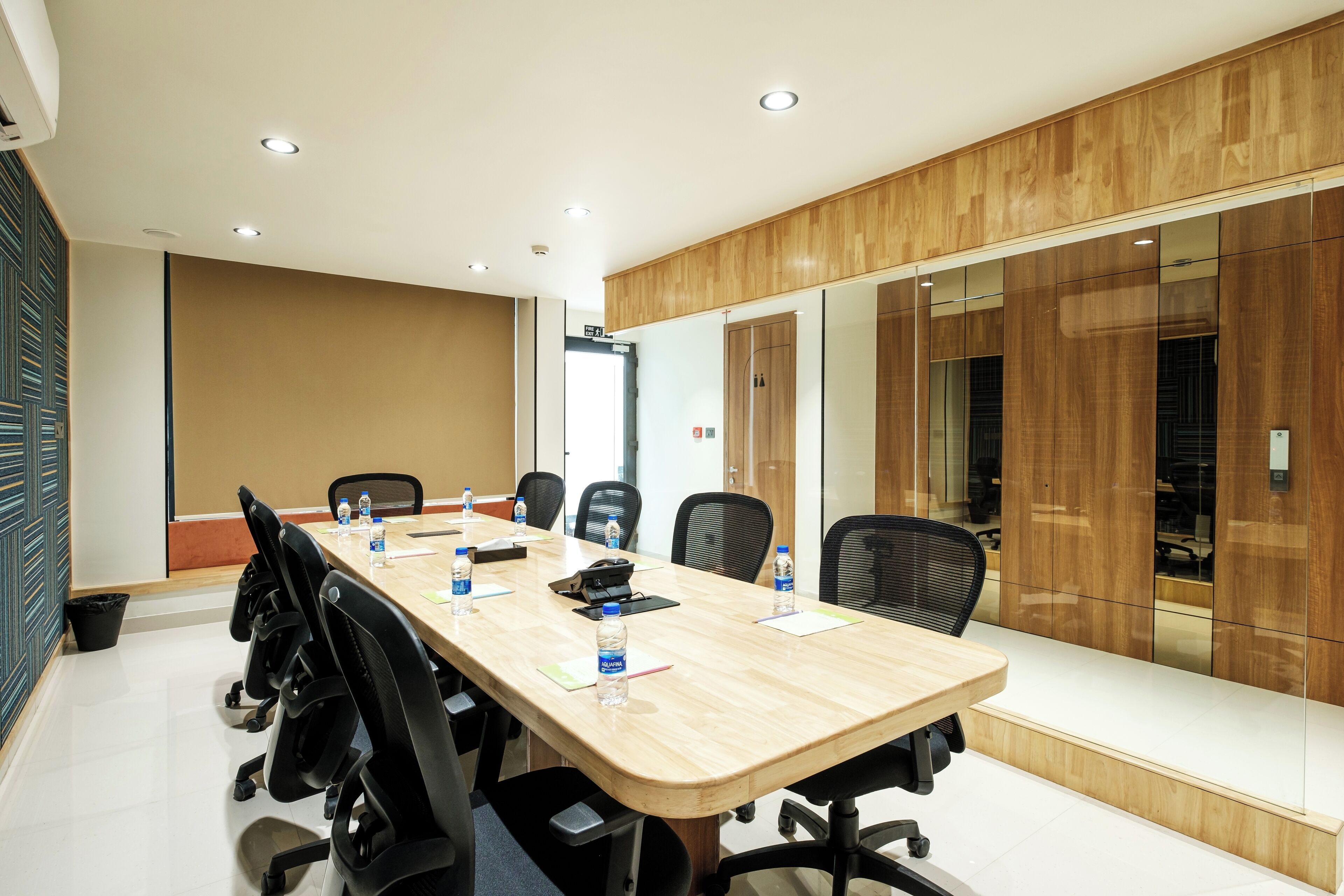 Ein Konferenzraum mit langem Tisch, schwarzen Bürostühlen und einer Wandpaneele aus Holz.