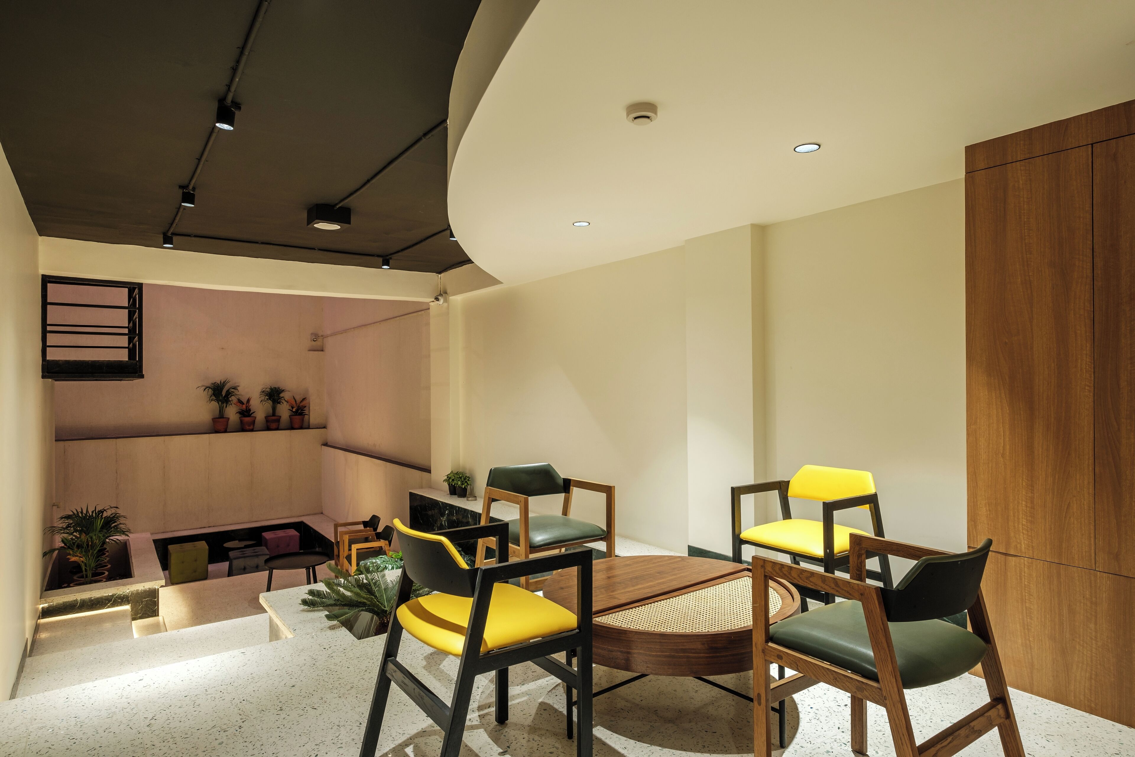 A modern dining area with a round table and chairs, a wooden cabinet, and a small seating area with a bench and plants.