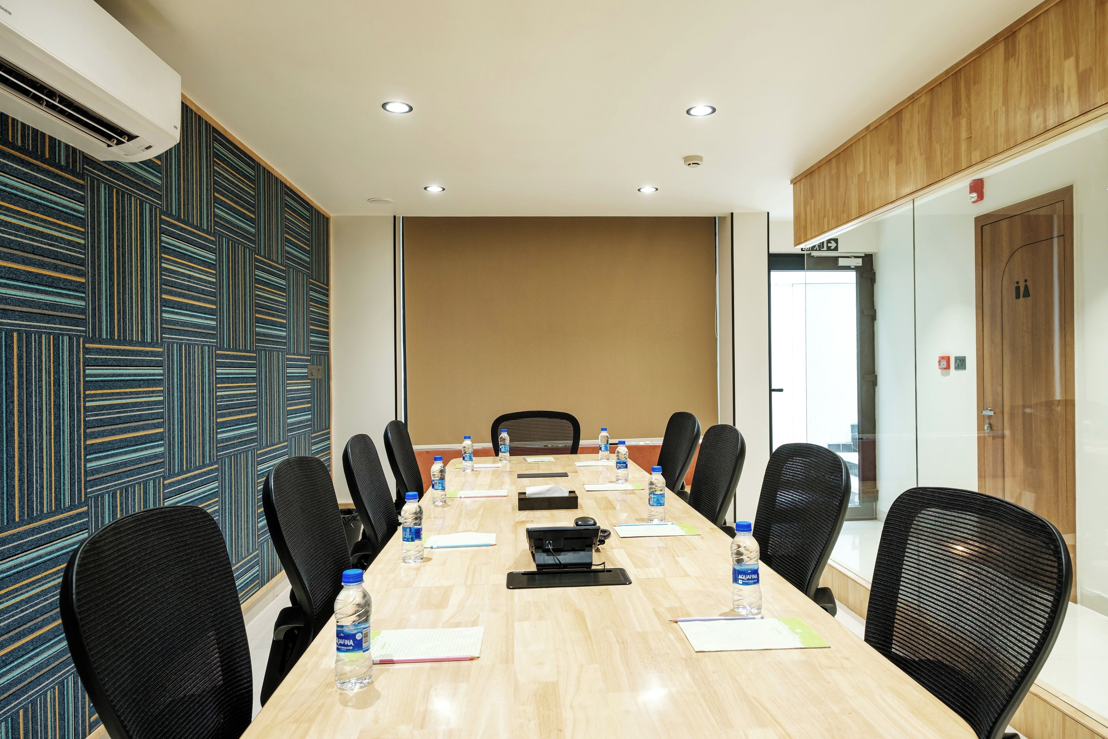 A conference room with a long table, black chairs, water bottles, and a projector.