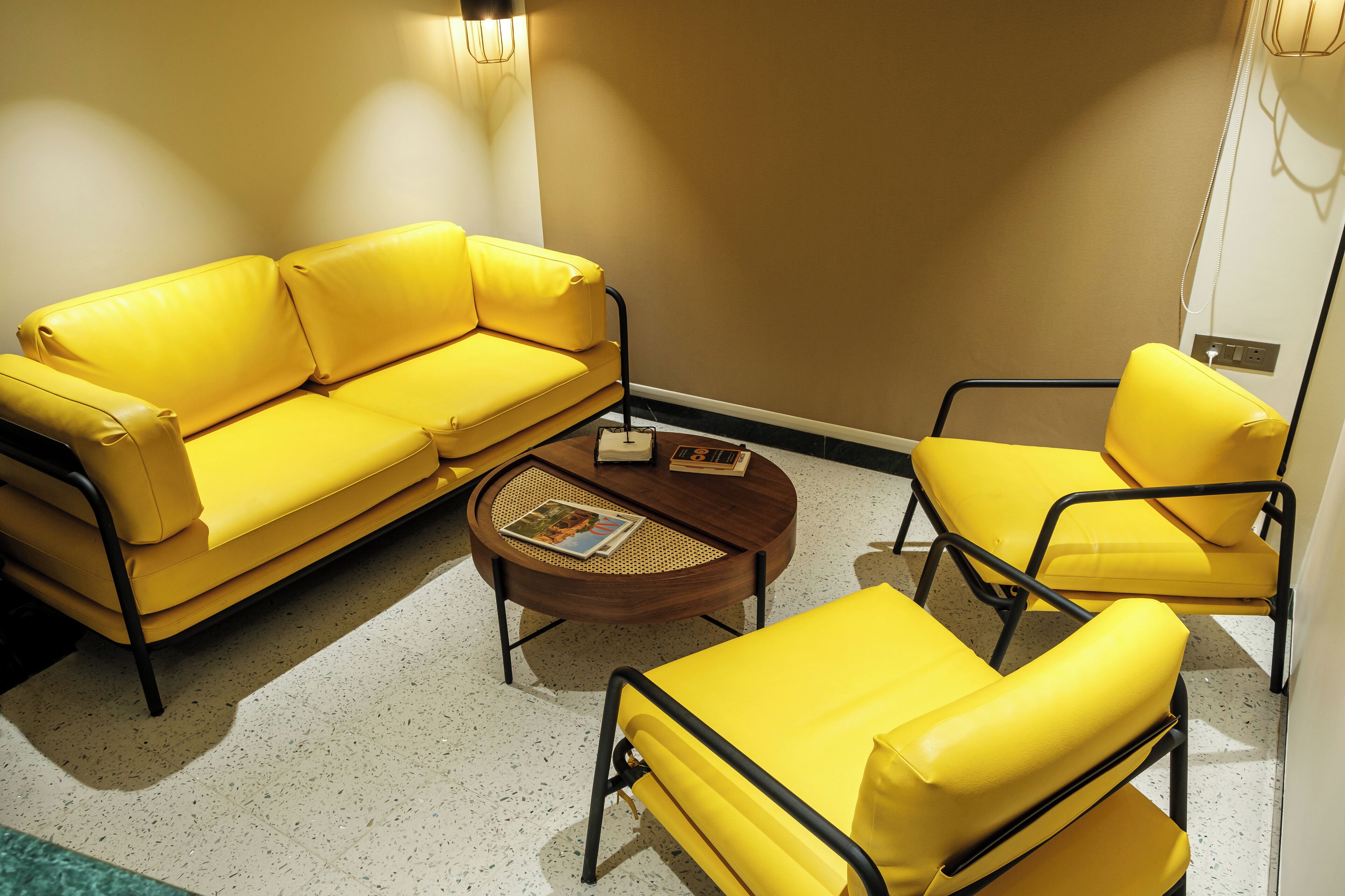 A yellow sofa set with a round coffee table, a small side table, and a wall-mounted light fixture.