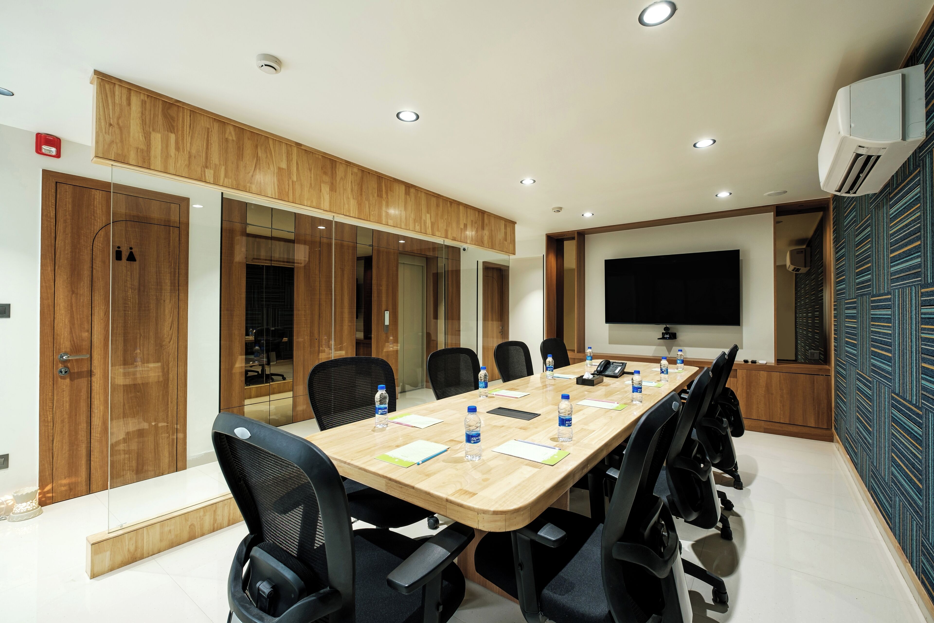 A conference room with a long table, chairs, a projector screen, and an air conditioning unit.