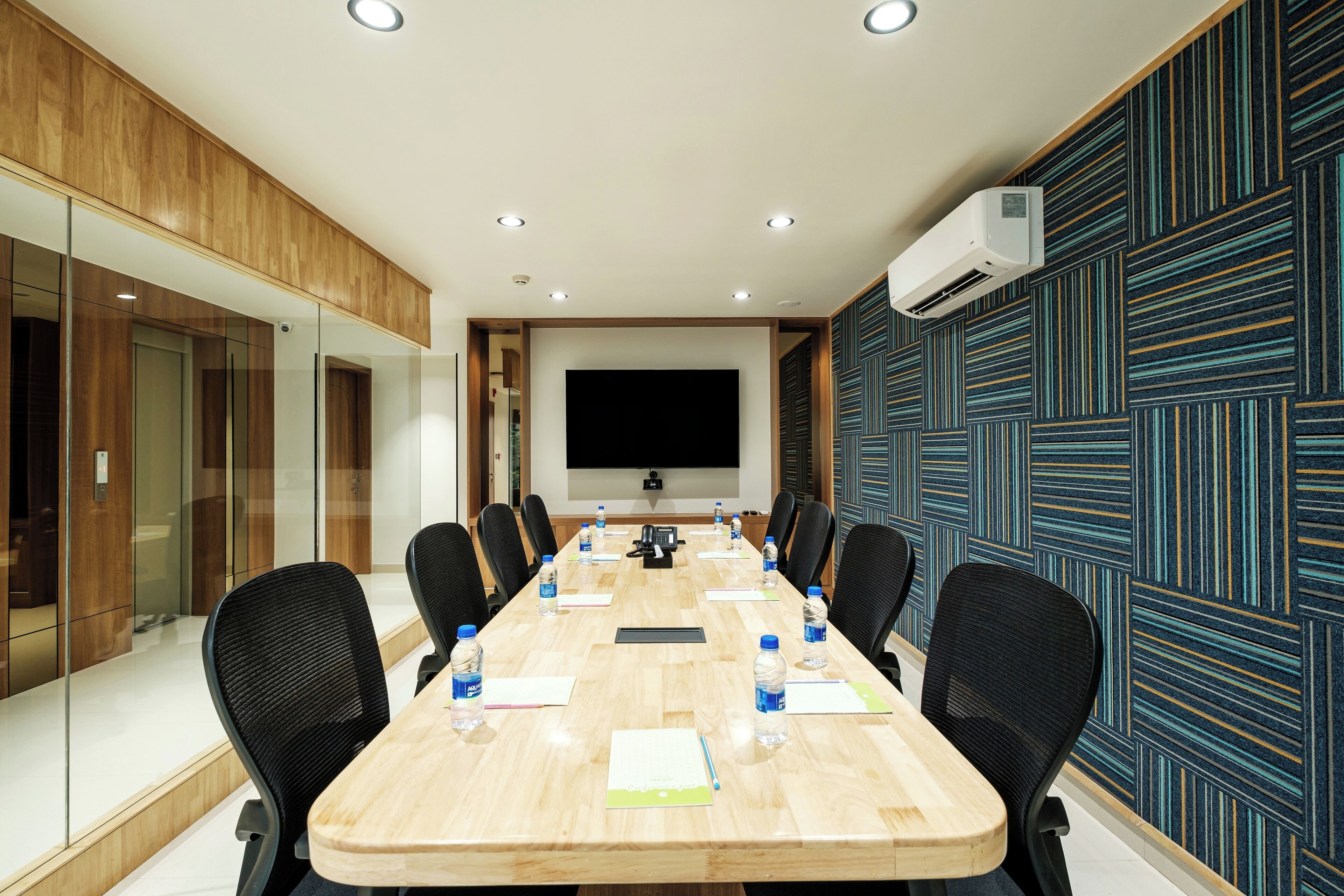 A conference room with a long table, chairs, a projector, and a large screen.