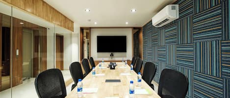 A conference room with a long table, chairs, a projector, and a large screen.