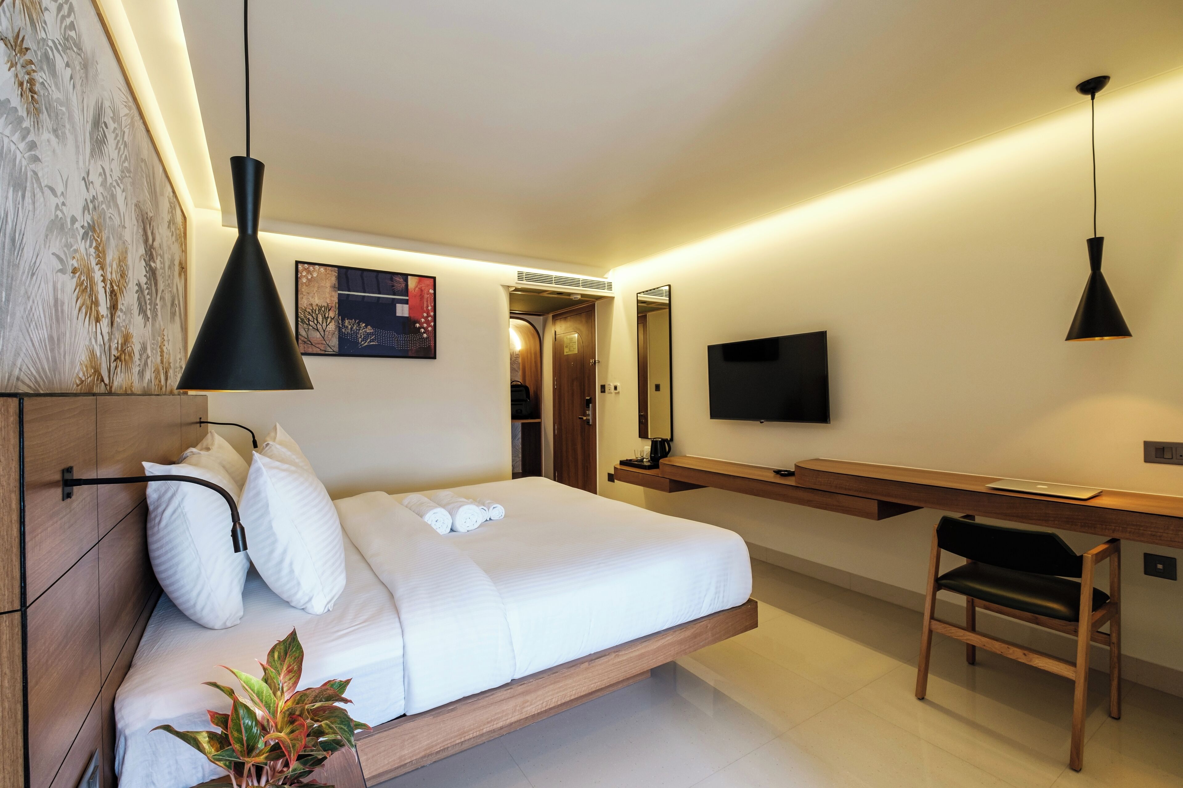 Quarto de hotel moderno com cama, mesa de cabeceira, escrivaninha, cadeira, televisão e obra de arte na parede.