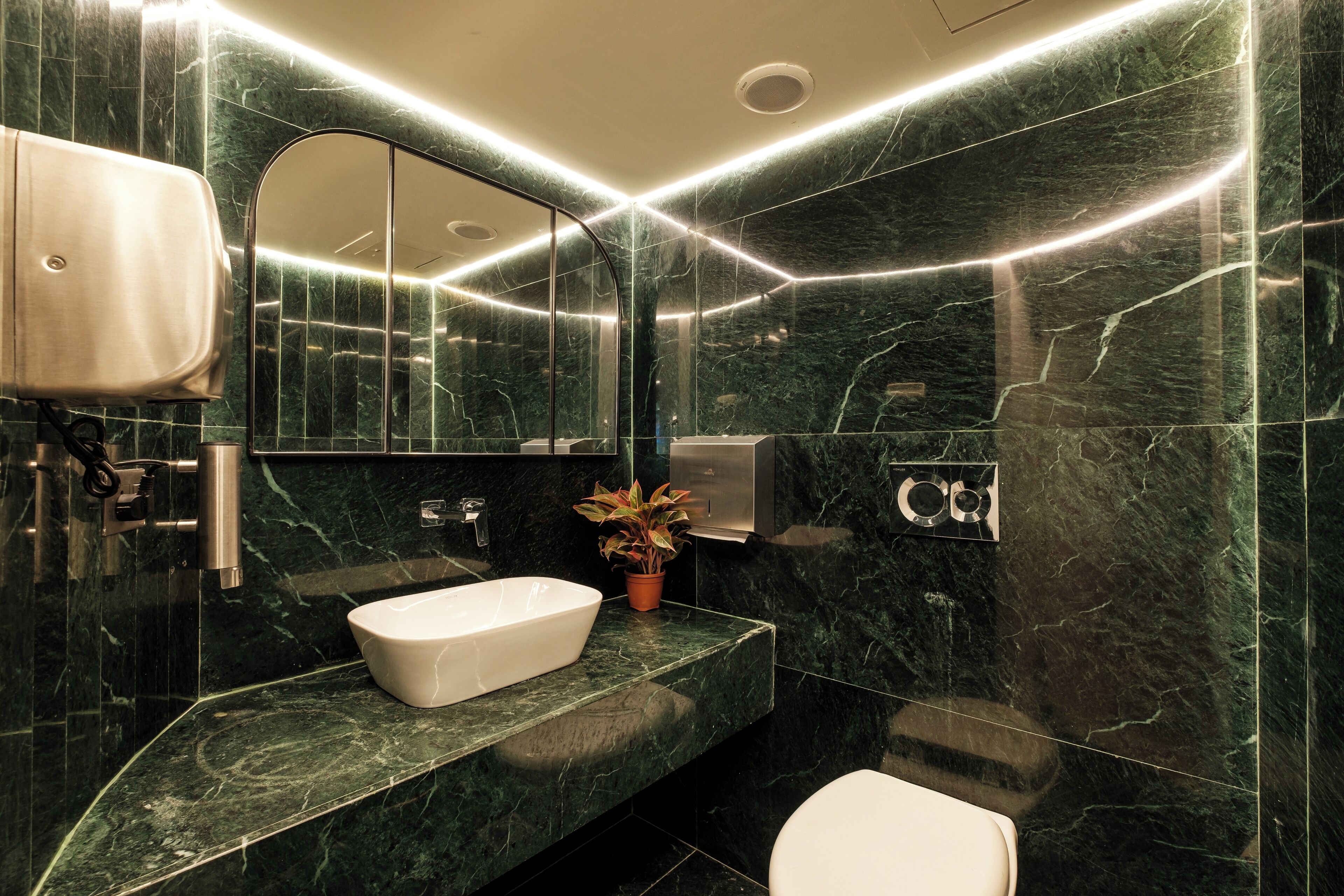Een moderne badkamer met een marmeren wastafel, een toilet en een handdroger.