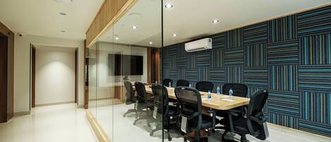 A conference room with a long table, black office chairs, and a glass partition.