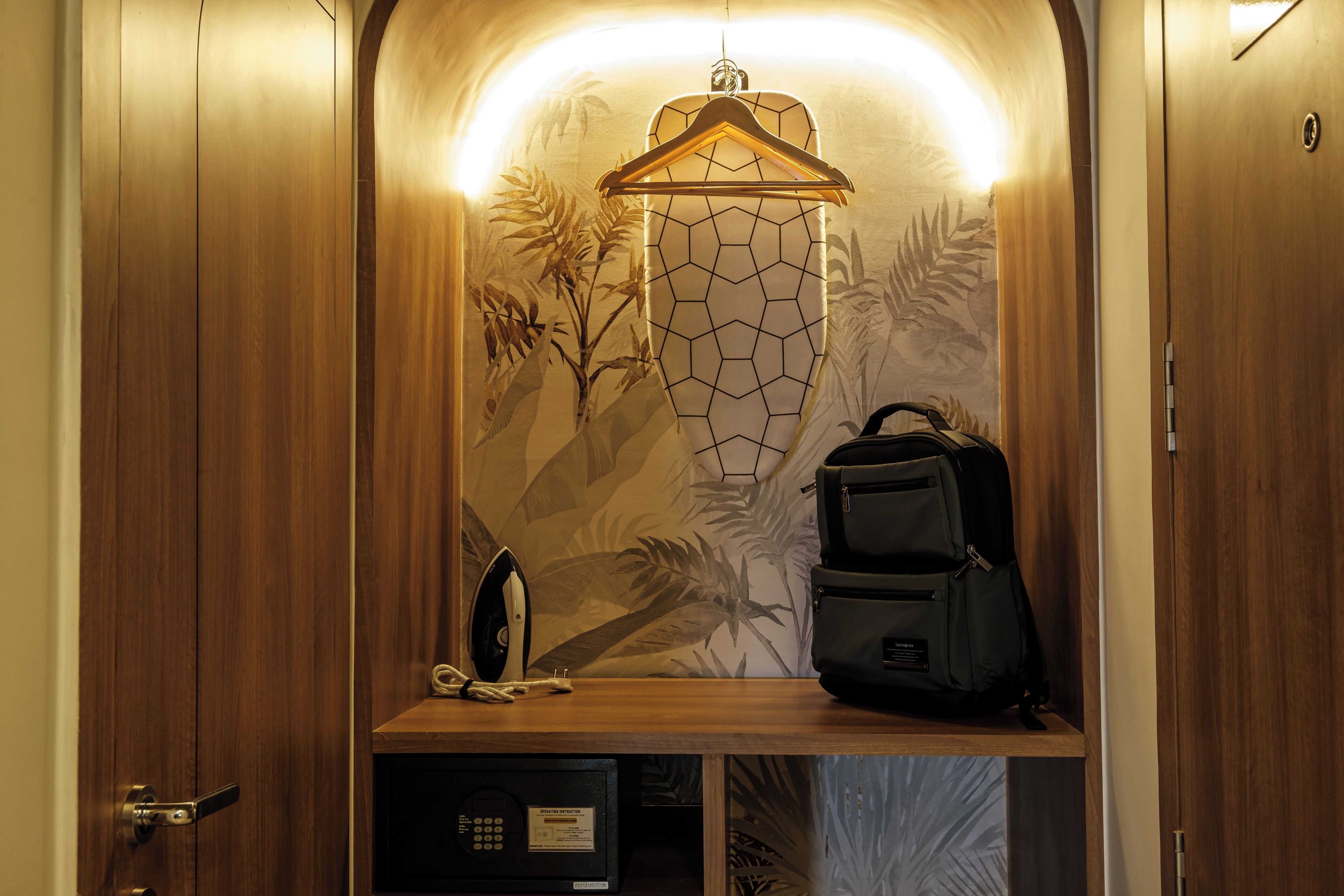 Un ascensor pequeño con interior de madera, un lámpara colgante, un perchero, una mochila negra y un estante con un teléfono y un microondas.