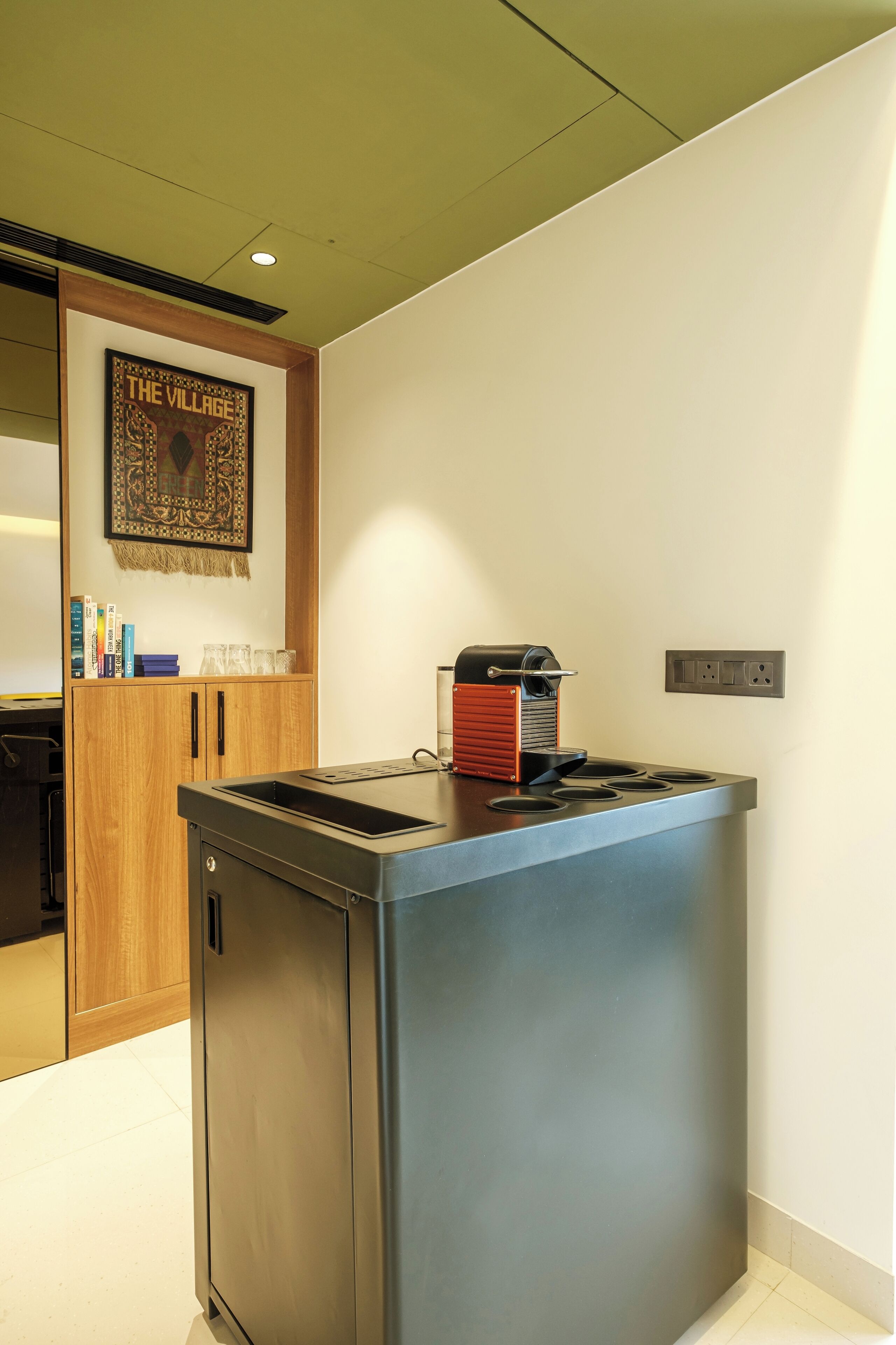 A compact kitchen with a built-in espresso machine, a wooden cabinet, and a wall-mounted power outlet.