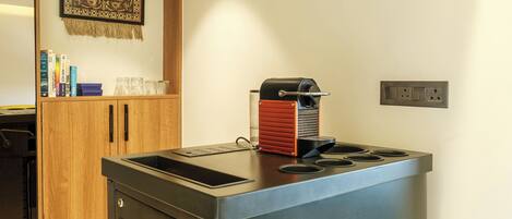 A compact kitchen with a built-in espresso machine, a wooden cabinet, and a wall-mounted power outlet.
